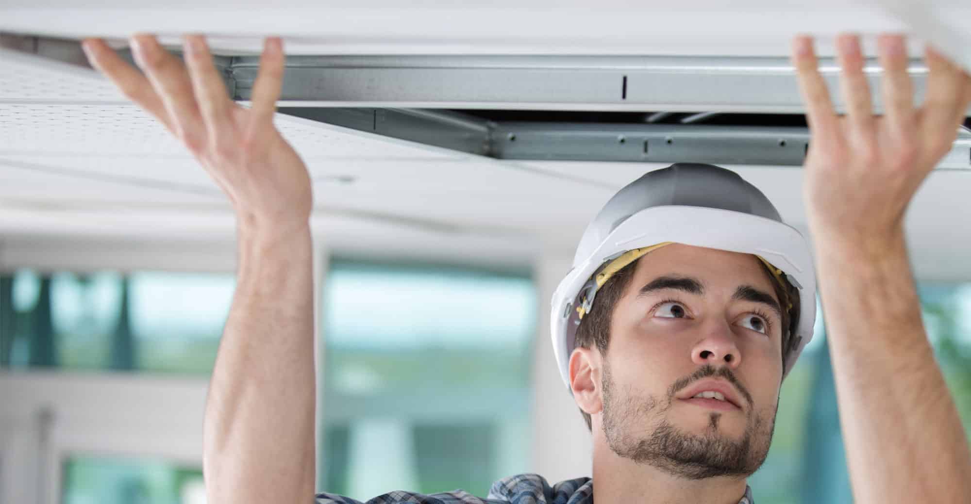 Technician opening a ceiling tile to work above the ceiling.
