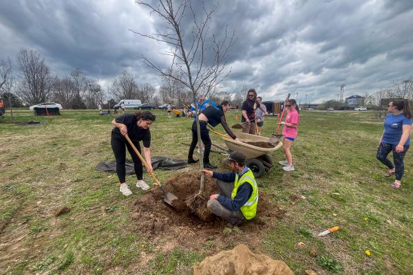 Arboriculture team member Nic Williamson helps students plant trees on campus
