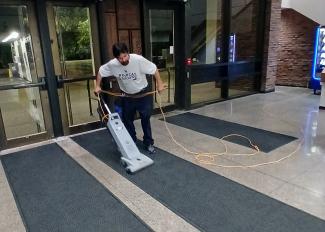 Custodial team member vacuums entrance rug