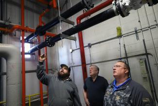 Three people stand in the Central Utility Plant looking at the integration of the rental deaerator tank
