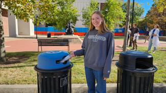A student throws a plastic bottle in an outside recycling container on campus