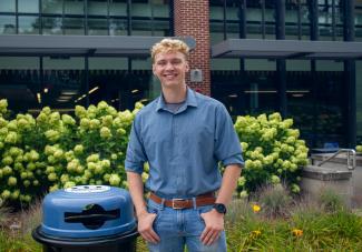 A student poses next to a recycling can on campus
