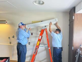Two men fix a light in a patient room in Good Samaritan Hospital