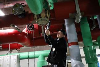 Facilities maintenance technician on a ladder looking at replacing a pressure reducing valve
