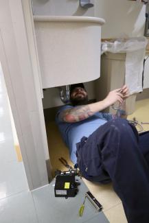 A facilities maintenance technician works under a sink