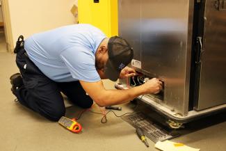 Facilities maintenance technician on the floor working to fix a hot box in the kitchen