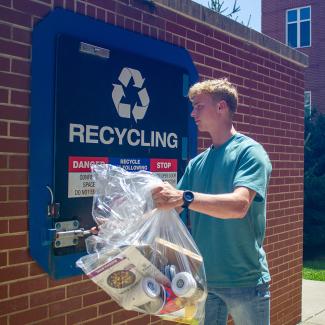 UK student throwing away recyclables in an outdoor compactor.