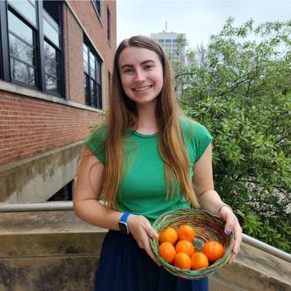 Elizabeth Hellmann holding up a wire basket of oranges.