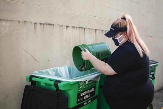 A starbucks employee emptying a small food waste bin into a larger container